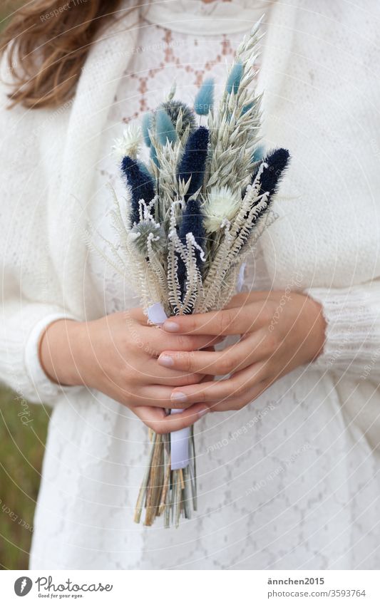 Eine Frau, es könnte eine Braut sein, hält einen Trockenblumenstrauss in der Hand Strauß Blumen Hochzeit Fest Feier heiraten Hände weiß weißes Kleid Jacke Wolle