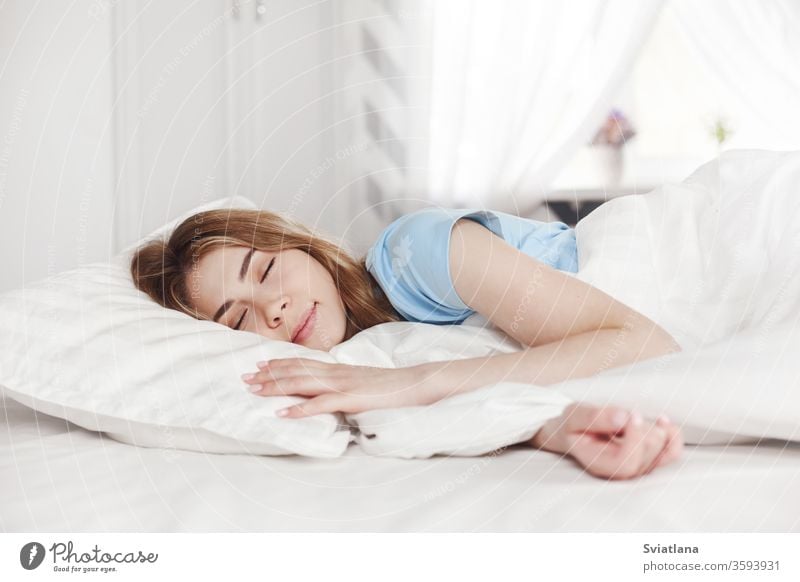 Ein schönes junges Mädchen in einem blauen Pyjama schläft morgens auf einem Bett in ihrem hellen Schlafzimmer zu Hause. Morgen Frau heimwärts schlafen