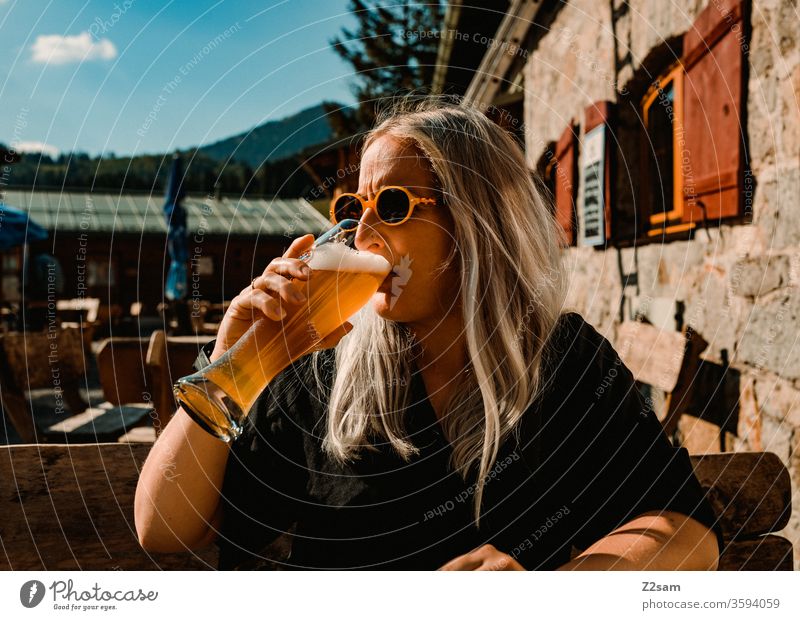 Junge Frau trinkt ein Weißbier auf der Almhütte almhütte berge gebirge alpen trinken genuß weißbier junge frau jugendlich blond lange haare sonnebrille