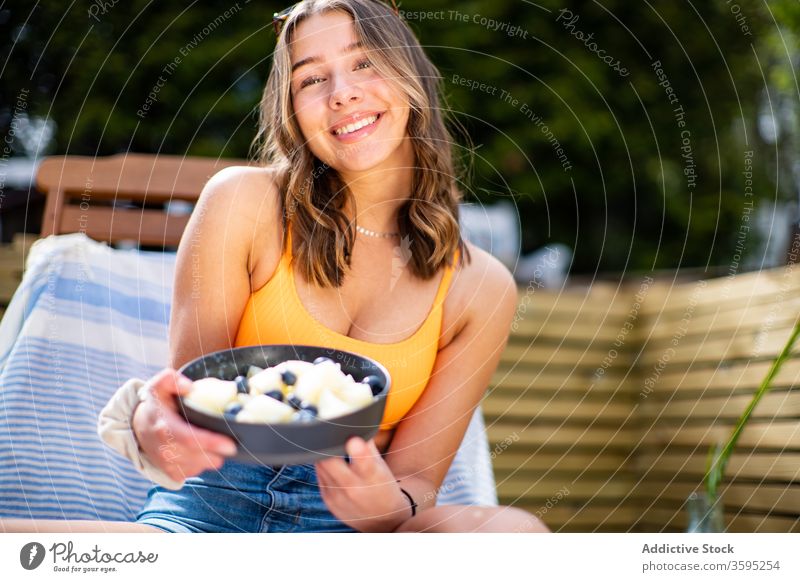 Lächelnde Frau mit Schale mit frischen Früchten Frucht Schalen & Schüsseln Sommer Kälte Beeren Liegestuhl Terrasse heiter sich[Akk] entspannen ruhen sitzen reif