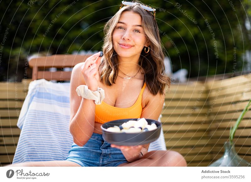 Lächelnde Frau mit Schale mit frischen Früchten Frucht Schalen & Schüsseln Sommer Kälte Beeren Liegestuhl Terrasse heiter sich[Akk] entspannen ruhen sitzen reif
