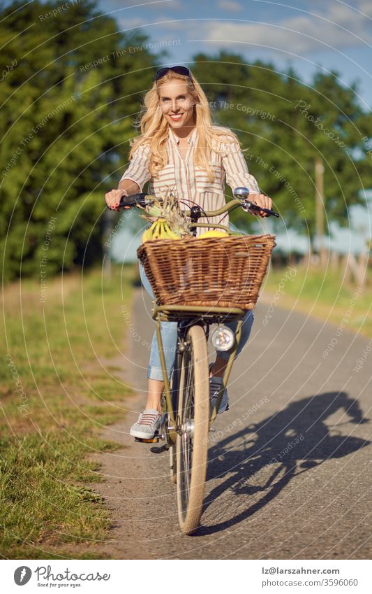Glückliche Frau lächelt beim Fahrradfahren mit einem Korb voller frischer und gesunder Früchte an einem sonnigen Sommertag auf dem Land Reiten Lächeln