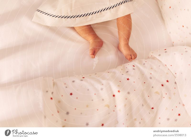 die Beine des Babys auf dem Bett. kleine Babybeine im Kleid. Ansicht von oben Hintergrund heimwärts Top Tochter neugeboren Baumwolle Decke Wollstoff weiß