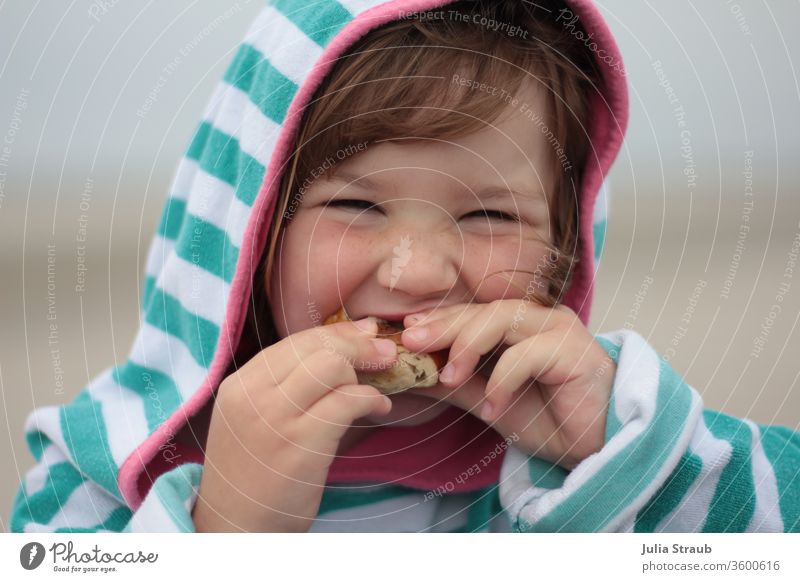 Mädchen mit Kapuzenhandtuch isst ein Brötchen Kleinkind Sommersprossen Handtuch grinsend Essen beißen halten semmel Laugenbrötchen gestreift Streifenpullover