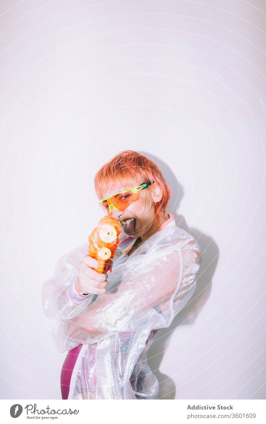 Retro-futuristische Frau, die eine Waffe auf die Kamera richtet Pistole zielen angriffslustig Stil jung Outfit retro Model Wasser Punkt gefärbtes Haar trendy
