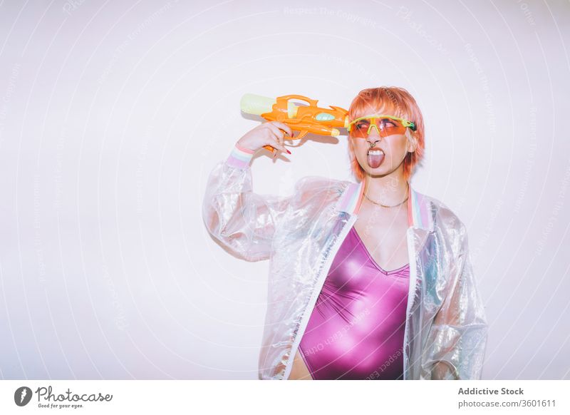 Lustige retro-futuristische Frau, die eine Pistole an den Kopf hält Stil Zunge zeigen lustig jung Waffe Outfit Model Wasser Spielzeug Punkt gefärbtes Haar