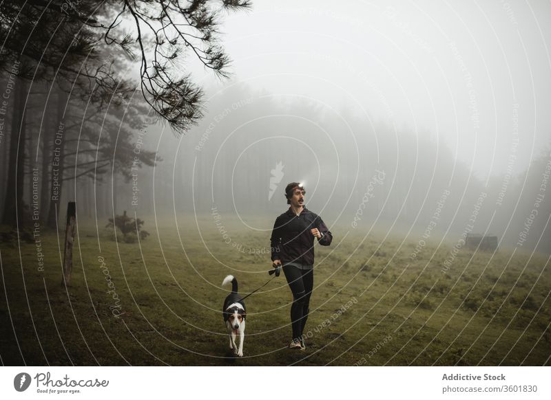 Fitnesssportler rennt mit Hund in nebligem Wald Läufer Sportler laufen Training joggen Jogger Nebel Holz männlich Sportbekleidung selbstbewusst Gesundheit