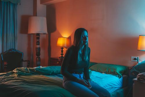 Junge Frau sitzt traurig auf dem Bett Porträt Nacht Quarantäne Depression Kopfkissen Coronavirus covid-19 Isolation selbstisoliert spät Schlafstörung blau