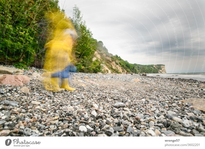 Ein schattenhaftes Wesen im Friesennerz läuft am Strand der Insel Rügen umher Schattenhaft Bewegungsunschärfe unscharf Mensch Kind Regenschutz Wetterschutz