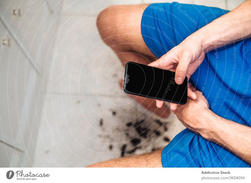Junger gesichtsloser Mann benutzt Smartphone, während er sich im Badezimmer ein Video zum Selbsthaarschnitt ansieht Haarschnitt Bildschirm zuschauen Gerät