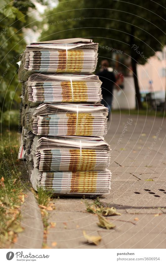 Stapel von Wochenzeitungen in Bündel warten auf dem Gehweg auf den Austräger. Im  Hintergrund bewegt sich ein Mensch weg. nebenerwerb Rentnerjob schülerjob