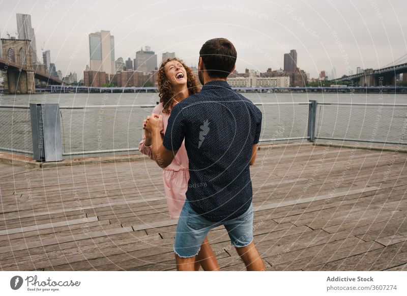 Glückliches Paar tanzt auf der Böschung Umarmen Spazierweg schlendern Großstadt heiter Tanzen Stauanlage Partnerschaft Fluss Umarmung Brooklyn Bridge Bewegung