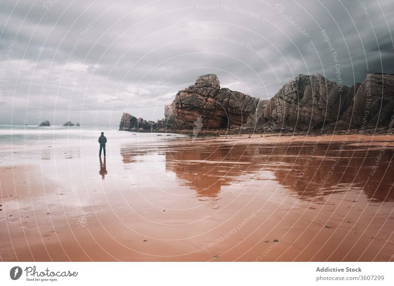 Einsamer Mann steht an sandiger Meeresküste mit felsigen Klippen Meeresufer Felsen rau Reisender MEER einsam bedeckt trist Natur Küste Reflexion & Spiegelung