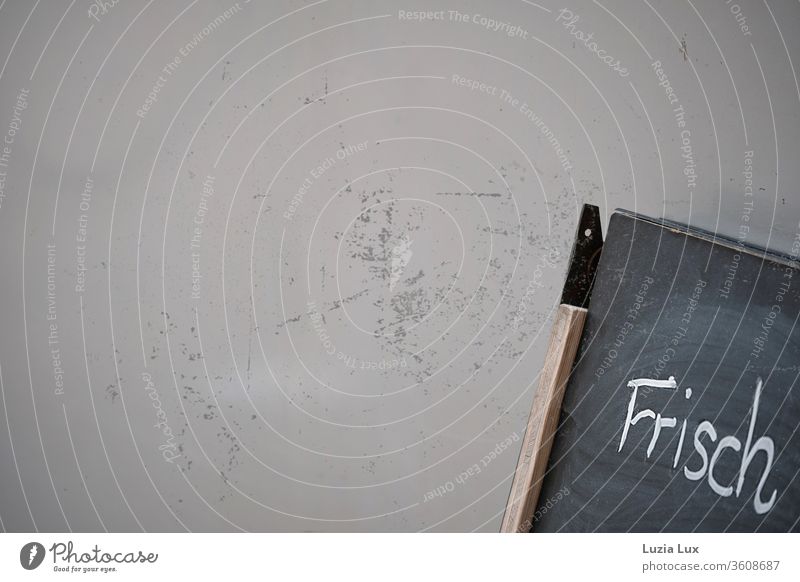 Frisch - ein angefangener Aufschrieb an einer Tafel, die an eine schmutzige Wand angelehnt steht Kreide Kratzer alt grau unfertig Farbfoto Menschenleer Holz
