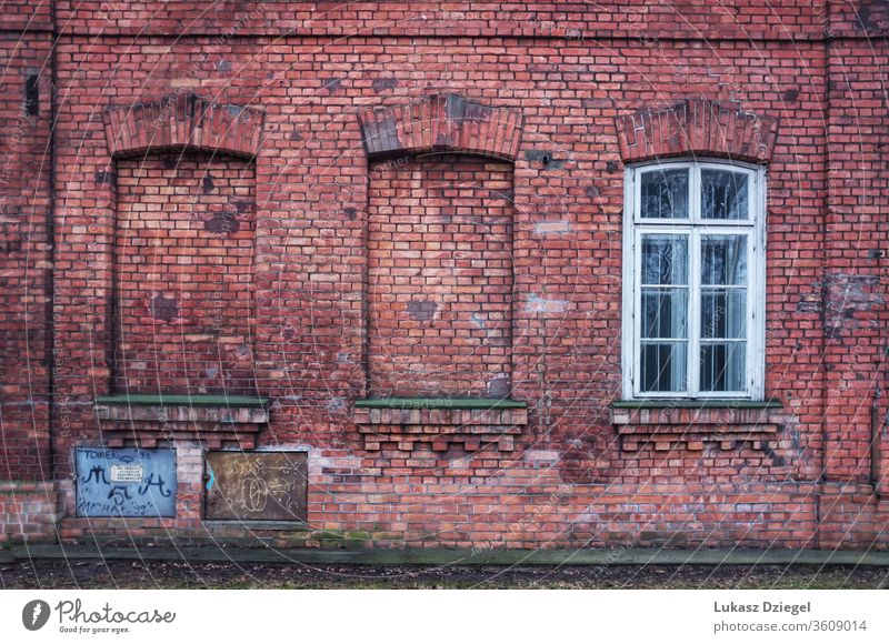 Die rote Backsteinmauer mit drei Fensteröffnungen, von denen zwei zugemauert wurden Material Wand mit Fenster verfallen altehrwürdig Rust rustikal retro