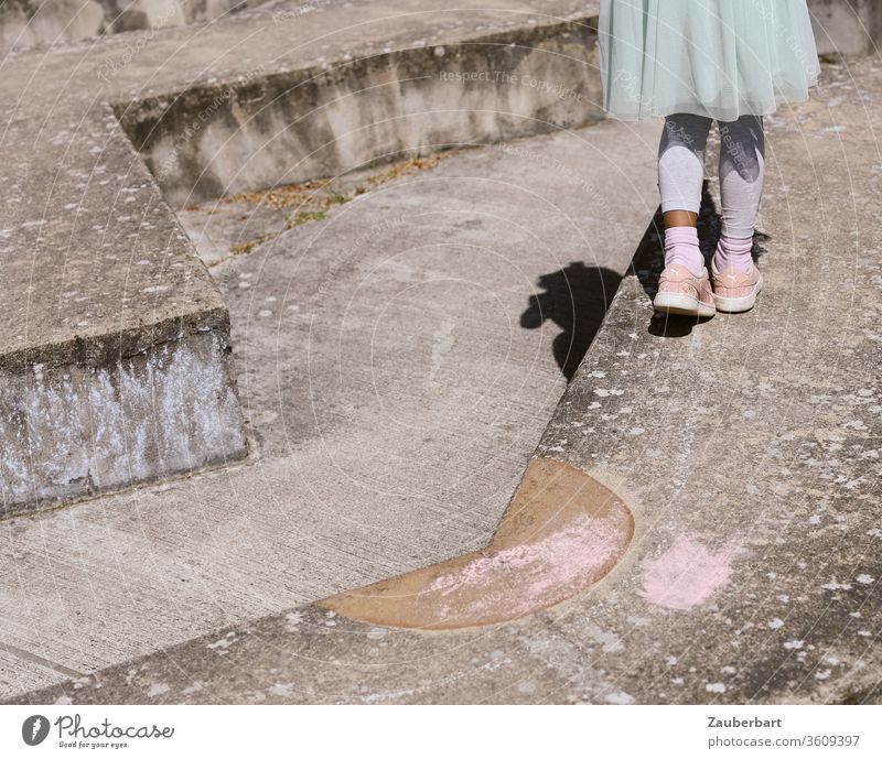 Beine eines Mädchens in rosa Sneakern und Tüllrock auf einer Bodenskulptur aus Beton Kind Skulptur Treppe Stufe Rück Labyrinth balancieren Balance Spielen