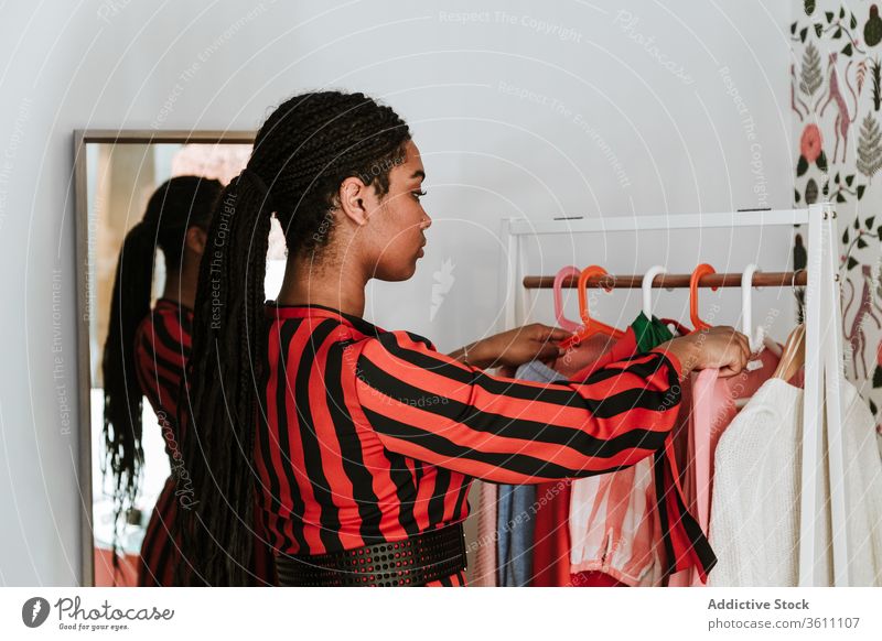 Modische schwarze Frau wählt Kleidung von der Stange Stoff heimwärts wählen Kleiderschrank Kleiderbügel Zopf Ablage Stil Mode stylisch pflücken Textil