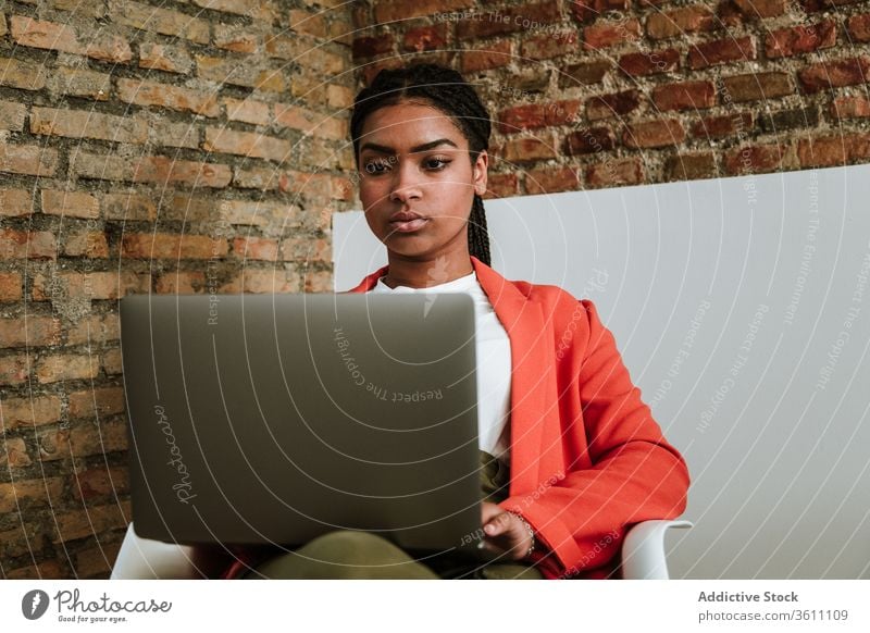 Moderne schwarze Frau mit Computer im Sessel Business Laptop online elegant Loft Design Fokus Innenbereich freiberuflich modern Gerät Apparatur Internet