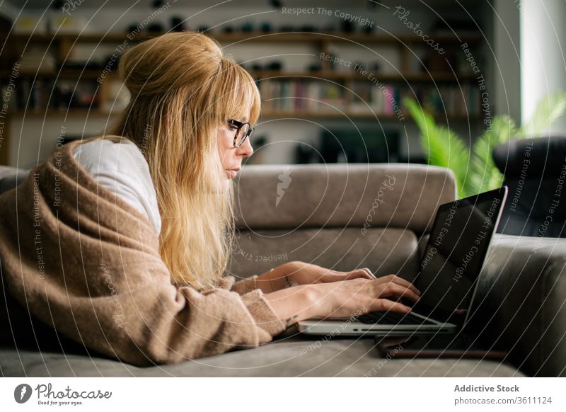 Nachdenkliche Frau arbeitet zu Hause am Laptop Browsen freiberuflich Projekt benutzend Telearbeit Lügen Sofa Arbeit abgelegen ernst Brille Apparatur Internet