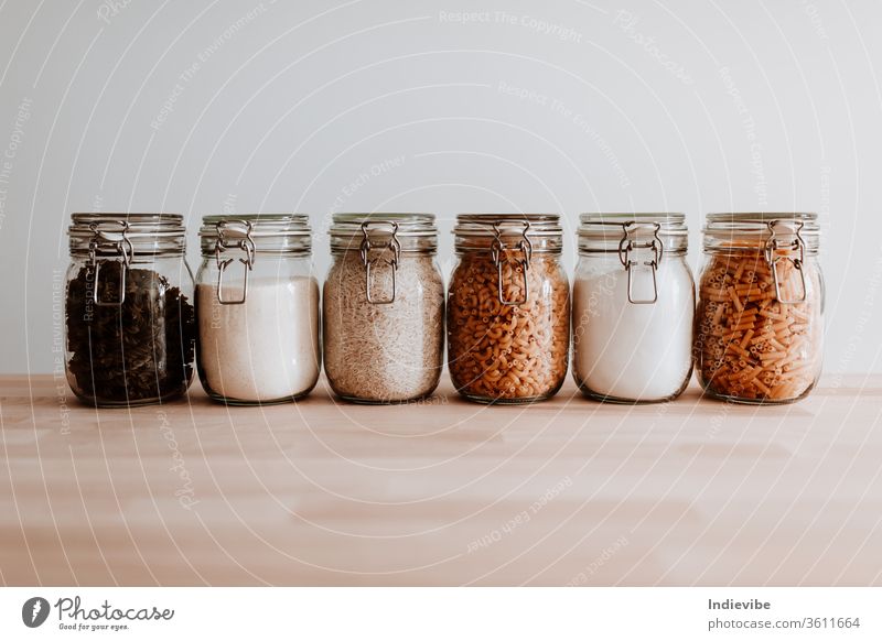 Sechs Gläser voll mit getrockneten ungekochten Lebensmittelzutaten. Nudeln, Reis, Mehl, Zucker. Glas Container weiß vereinzelt Gesundheit Bestandteil Küche