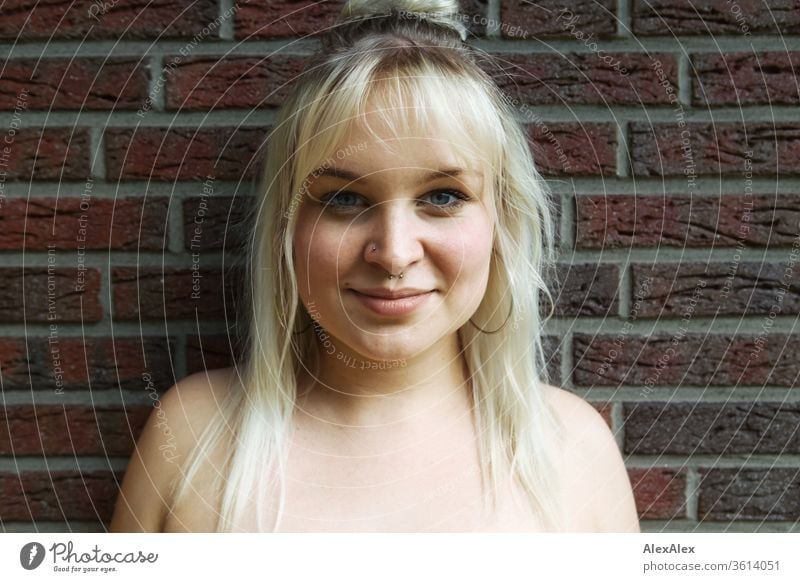 Portrait einer jungen blonden Frau vor einer Backsteinwand Mädchen junge Frau schön lächeln lange Haare Ohrringe blaue Augen Haut 19 18-20 Jahre 15-20 Jahre alt