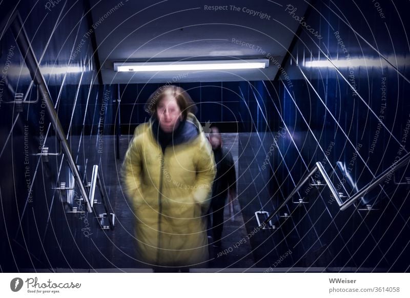 U-Bahn Übergang, Frau wird von Mann verfolgt Tunnel Treppe dunkel verfolgen Angst Furcht Unsicherheit Gefahr unsicher ängstlich gruselig gefährlich blau