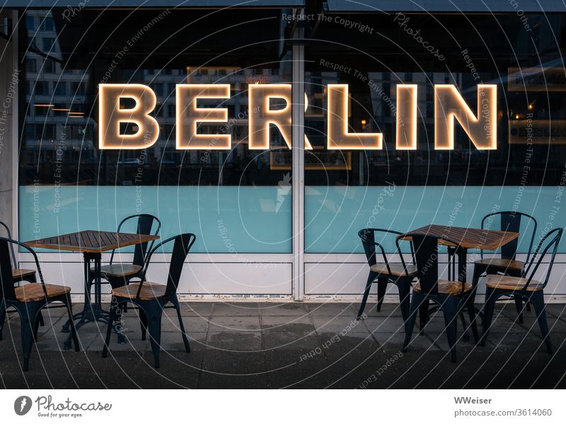 Café mit leuchtendem Berlin-Schriftzug, Abendlicht Straßencafé Stühle Tische leer Gastronomie Restaurant Außenaufnahme Tourismus Lifestyle regnerisch