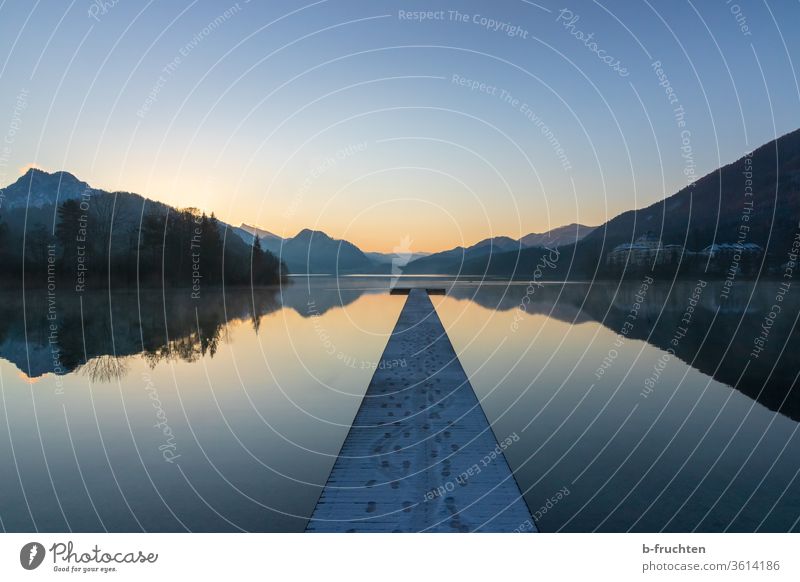 Morgendämmerung am Gebirgssee, Winter See Steg Holzsteg Spiegelung Spuren Kalt Gebirge Alpen Ruhe ruhig entspannung Wasser Landschaft Natur