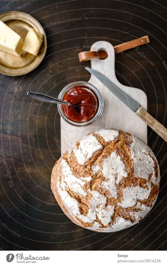 Ein Laib Brot, ein Glas mit Marmelade und Butter auf einem goldenen Teller, rustikaler Stil Frühstück Schneidebrett Draufsicht Lebensmittel gebacken lecker süß