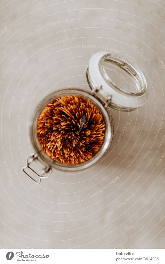 Nahaufnahme eines mit ungekochten Spaghetti-Nudeln gefüllten Glasbehälters auf grauem Hintergrund Lebensmittel Container Vorratskammer luftdicht Grundlagen