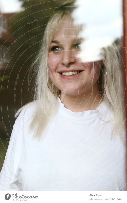 Portrait einer jungen blonden Frau hinter einer Fensterscheibe Mädchen junge Frau schön lächeln lange Haare blaue Augen Haut 19 18-20 Jahre 15-20 Jahre alt fit