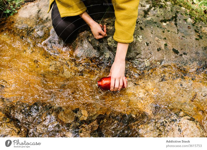 Anonyme Frau, die Wasser aus einem Bach im Wald entnimmt ruhen Flasche Sauberkeit Stil grün Oberbekleidung Natur sich[Akk] entspannen Lifestyle Landschaft