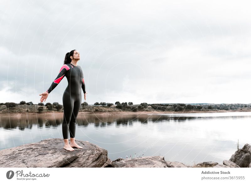 Inspirierte Sportlerin auf hohem Felsen gegen See Frau Neoprenanzug Taucher Wasser Felsbrocken Abend Inspiration Sonnenuntergang Badeanzug Natur Ufer