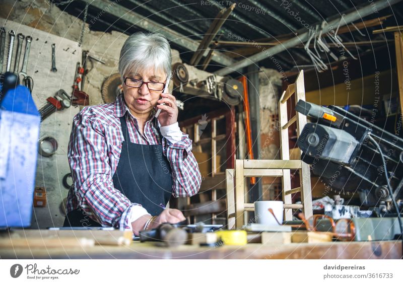 Zimmermannsfrau in ihrer Werkstatt Frau Zimmerer Senior sprechend Mobile maßgefertigt Business Taille hoch Schreinerei Werkbank reif schreibend Holz Arbeiter