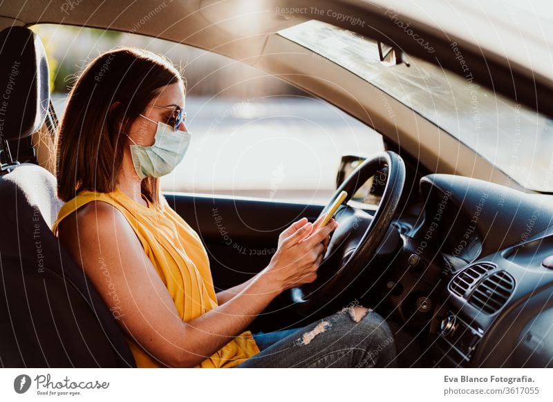 junge Frau in einem Auto, die ein Mobiltelefon benutzt und eine Schutzmaske trägt. Sommersaison. Konzept zur Prävention des Coronavirus PKW Handy Virus