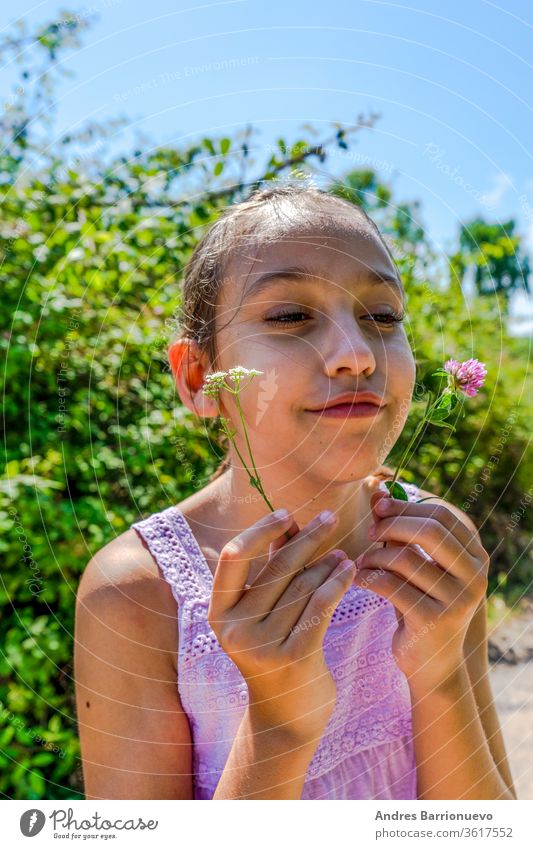 Hübsches kleines Mädchen mit einer Maske, um sich vor dem Coronavirus zu schützen, das auf einem Pfad inmitten der Natur eine Blume pflückt sich[Akk] entspannen