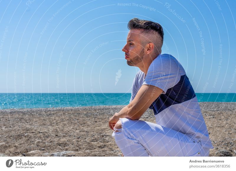Junger Mann in weißer Hose und modernem Styling posiert am Strand des Mittelmeers in Burriana Vergnügen Feiertag getönt Mode Himmel Tourist Pose Wind Bräune