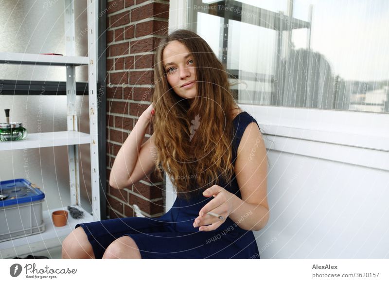 Junge Frau sitzt auf ihrem Balkon, lächelt und raucht eine Zigarette junge Frau Jugendliche feminin schön Gesicht 18-30 Jahre Mensch Farbfoto