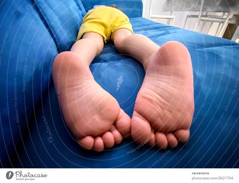 die Fußsohlen eines Kindes, das auf einem blauen Sofa auf dem Bauch liegt. Baby Kindheit Barfuß Sohle Faulheit horizontal Liege gelb Tag niedlich Körper Pflege