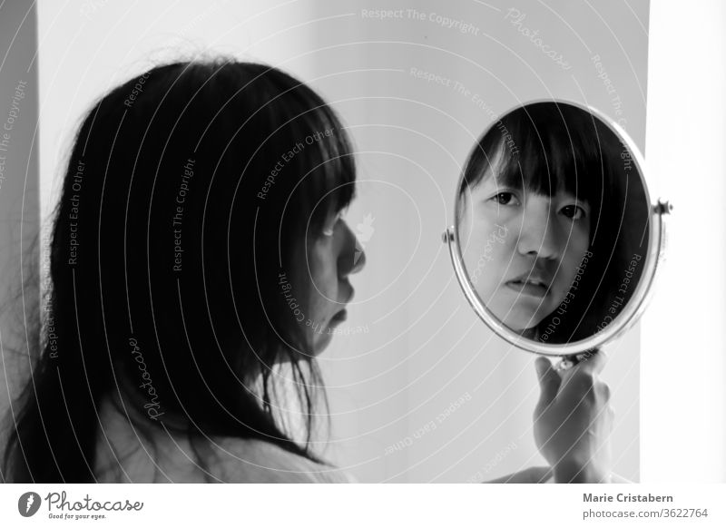 Asiatische Frau, die im Spiegel ihr Spiegelbild betrachtet Selbstliebe Konzeptionelles Porträt Spiegelreflexion Mensch feminin Junge Frau Zentralperspektive