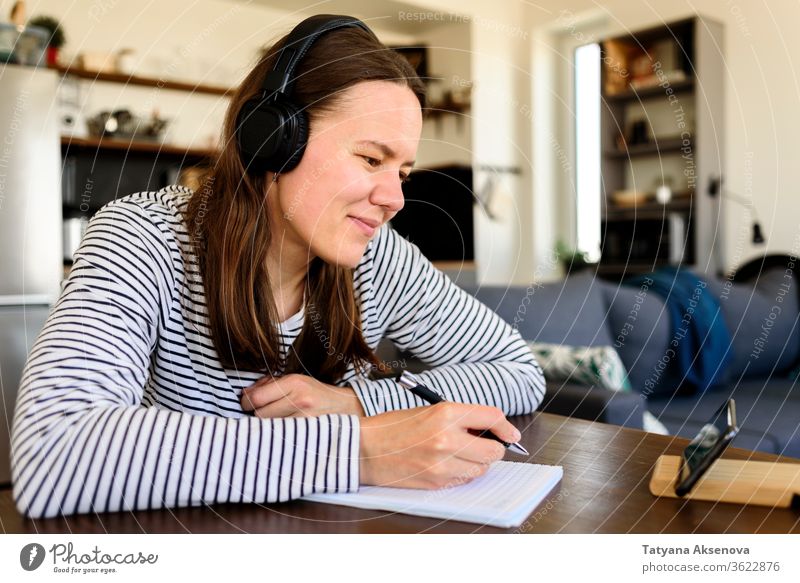 Frau mit Kopfhörern lernt zu Hause Bildung online Lernen E-Learning heimwärts Entfernung zuschauend hören Schüler Hausaufgabe Internet studierend