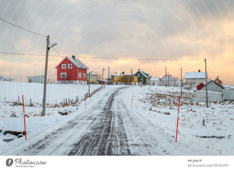 verschneite Straße in Norwegen auf den Lofoten im Winter mit viel Schnee und Eis und kalt ist es auch richtig eisig und frostig auf der leeren Straße mit dem Laternenpfahl und den Schneemarkierungen - ist bestimmt auch glatt -Wolken sind auch am Himmel