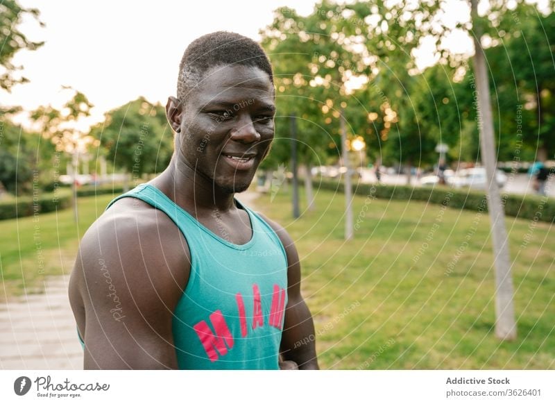 Porträt eines sportlichen schwarzen Mannes im Park Afrikanisch heiter muskulös Fitness Lächeln stark Biegung Körper passen Muskel Bizeps Glück Waffen Athlet
