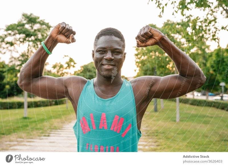 Athletischer schwarzer Mann trainiert im Park Afrikanisch heiter muskulös Fitness Lächeln stark Biegung Körper passen Muskel Bizeps Glück Waffen Stärke