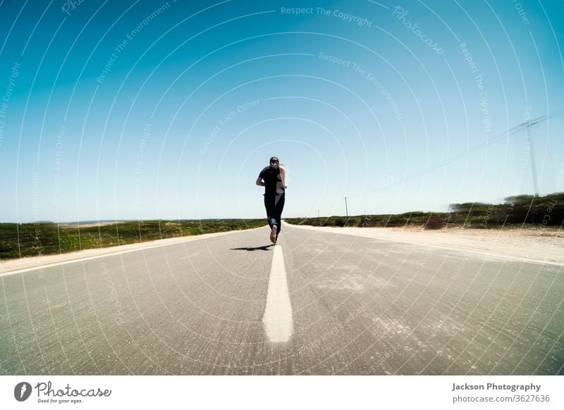 Ein Mann rennt mitten auf der leeren Straße Läufer laufen Textfreiraum Asphalt Konzept Linie Fuß barfüßig unverhüllt Bewegung verschwommen ausgerissen Portugal