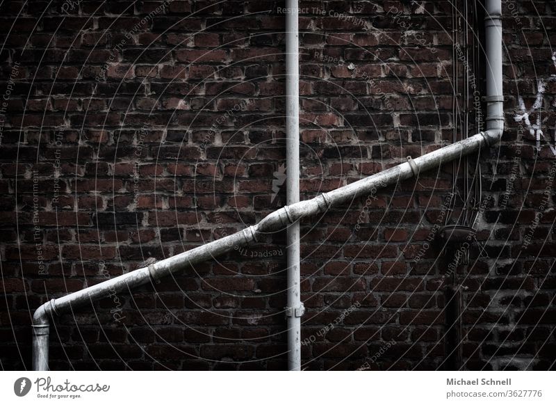 Sich kreuzende Wasserrohre an einer alten Hauswand aus Backsteinen Rohre Leitung Wand Menschenleer Mauer Metall Farbfoto Außenaufnahme Fassade Detailaufnahme