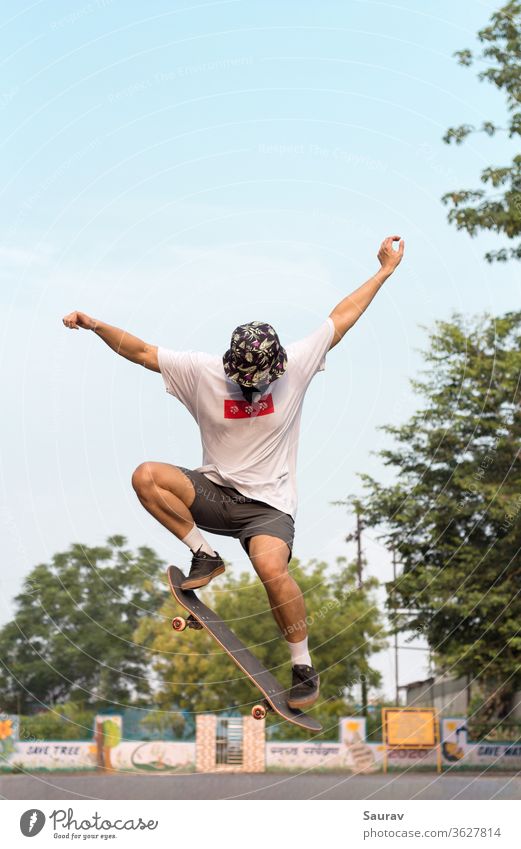 Ein junger Erwachsener, der eine Schutzmaske trägt, um eine Infektion mit dem Coronavirus zu vermeiden, während er einen Ollie-Stunt auf seinem Skateboard im Freien auf einer leeren Straße macht.