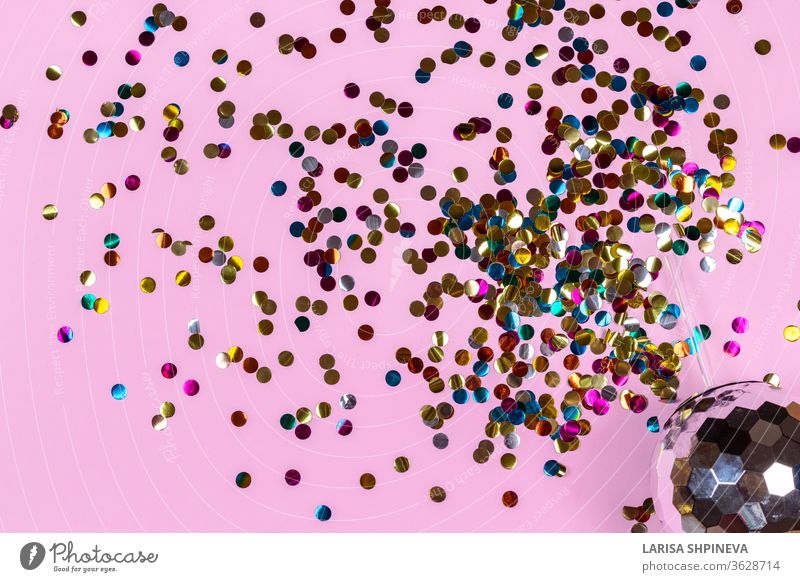 Kreative Kugeltasse in Form eines Disco-Cocktails mit Blitzeffekt, die funkelt und goldfarbenes Konfetti auf rosa Hintergrund versprüht. Konzept für Feiertage und Partys. Draufsicht, Flachlegung, Kopierraum