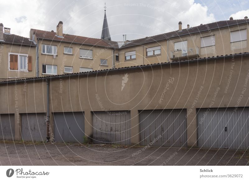 Typischer Hinterhof einer Kleinstadt in Lothringen mit Autogaragen Häusern Kirchturm und Mensch mit Handy Fassaden Himmel Wolken Fenster grau