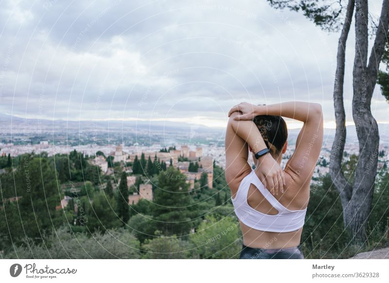 Fitte Frau im Urlaub bei Dehnübungen über der Stadt am Sommernachmittag vor der Alhambra. Fitness Lifestyle Übung Sonnenuntergang Spanien saubere Luft eine